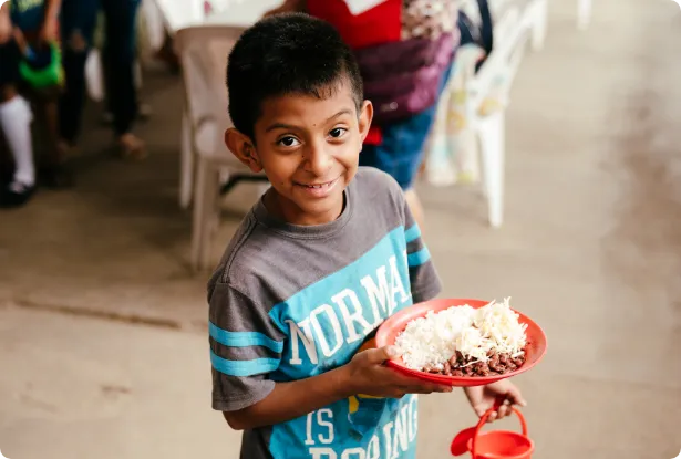 Smiling child holding a plate of food at an ORPHANetwork feeding program